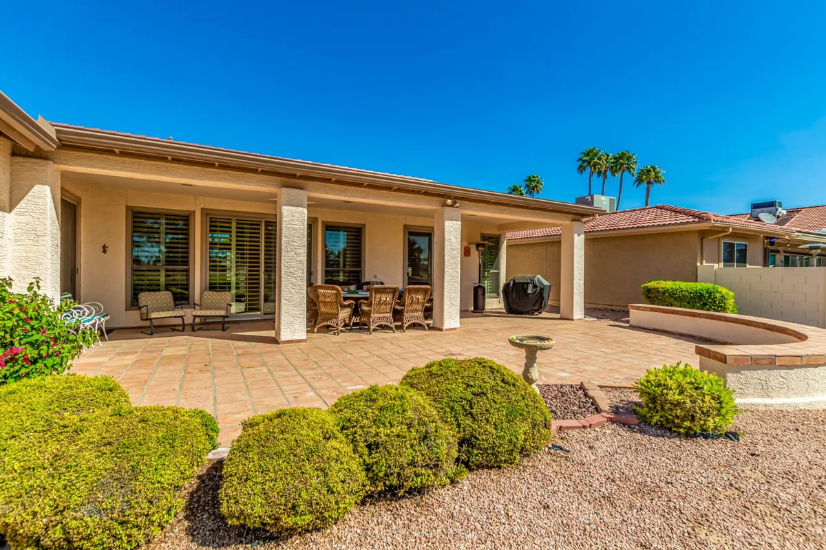 A stylish outdoor patio set with a dining table and chairs, lush landscaping, and sunlight streaming across the space. The setup encourages group meals, relaxation, and social gatherings with friends or family.