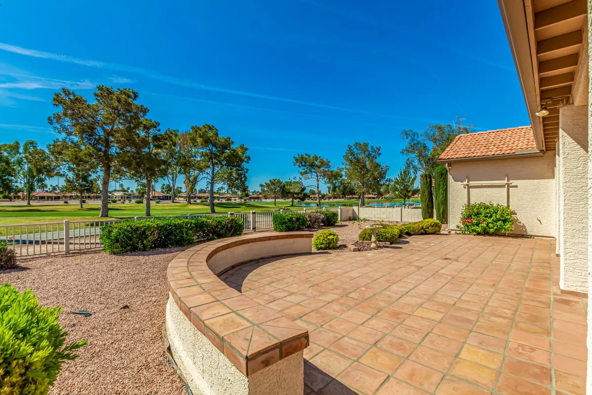 The image shows a spacious patio overlooking a lush green landscape and a sweeping view of the golf course. The patio is designed for both relaxation and al fresco dining, with comfortable seating and plenty of space for group gatherings. The tranquil atmosphere is accentuated by the soft light of a sunset or morning glow, inviting extended conversations and leisurely meals.