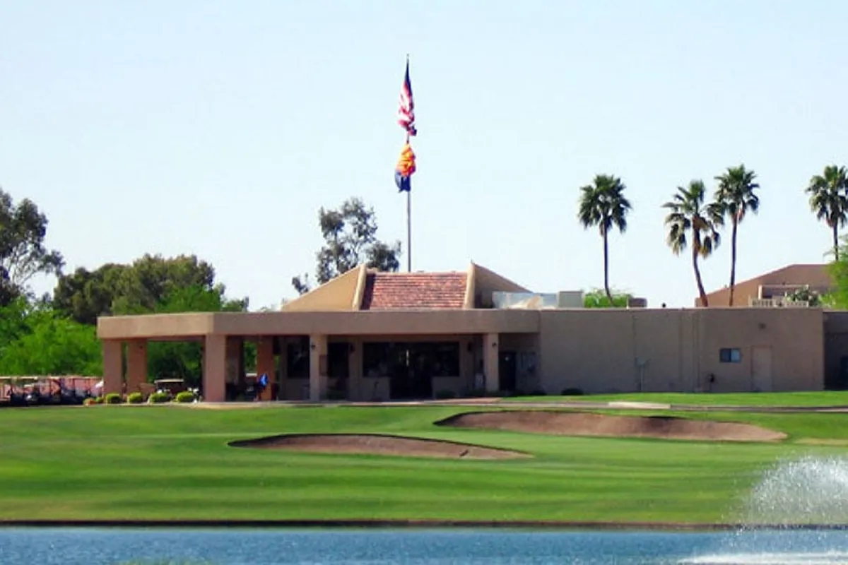 This image showcases a sweeping view of a lush golf course with a prominent clubhouse, surrounded by manicured greenery and a flag pole in the foreground. The setting exudes a relaxed, social vibe that encapsulates the heart of country club living: golf, gathering, and community events.