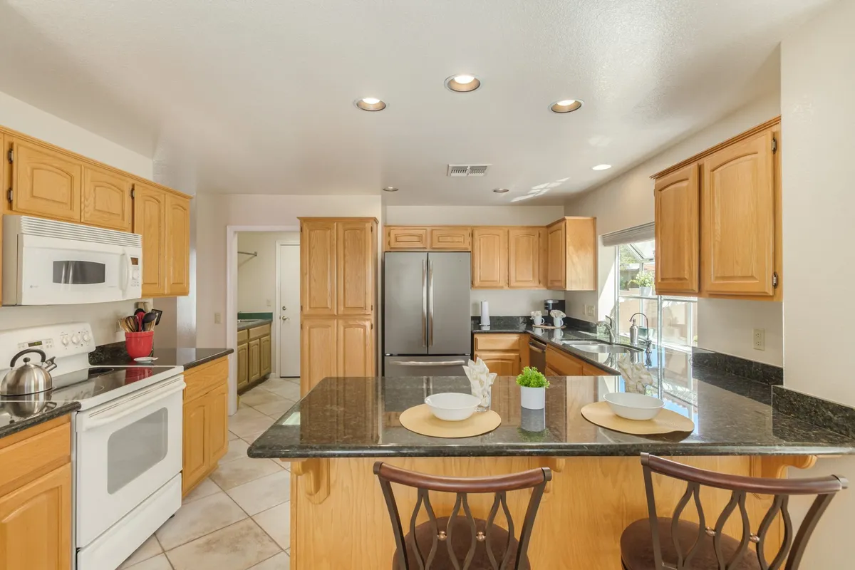 A warmly lit kitchen with granite countertops, oak cabinetry, and stainless steel appliances. The kitchen island offers space for meal prep or casual conversation, and the overall layout is open, inviting, and well-equipped for both daily use and entertaining.