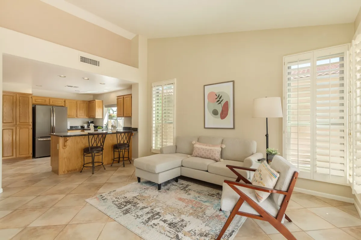 An inviting open-plan living space where a comfortable sofa and armchair are oriented toward a kitchen island visible in the background. The arrangement encourages conversation and easy movement between cooking, relaxing, and entertaining.