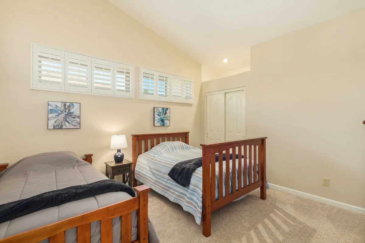 A guest bedroom featuring two beds with decorative wall art above, a table lamp, and a comfortable, intimate feel—ideal for accommodating friends or family.