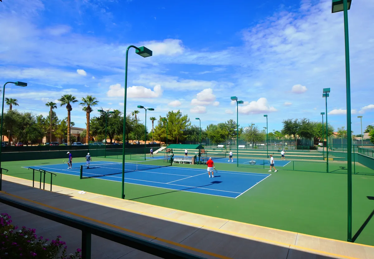 This exterior shot captures well-maintained tennis courts lined with palm trees, with active players engaged in a match. The environment is energetic and social, reinforcing the daily recreational opportunities available in the community.