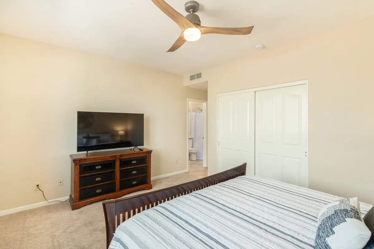 A cozy bedroom with striped bedding adorning a plush bed, a wooden dresser, a flat-screen TV, and a ceiling fan. The space feels tranquil, comfortable, and ideal for winding down.