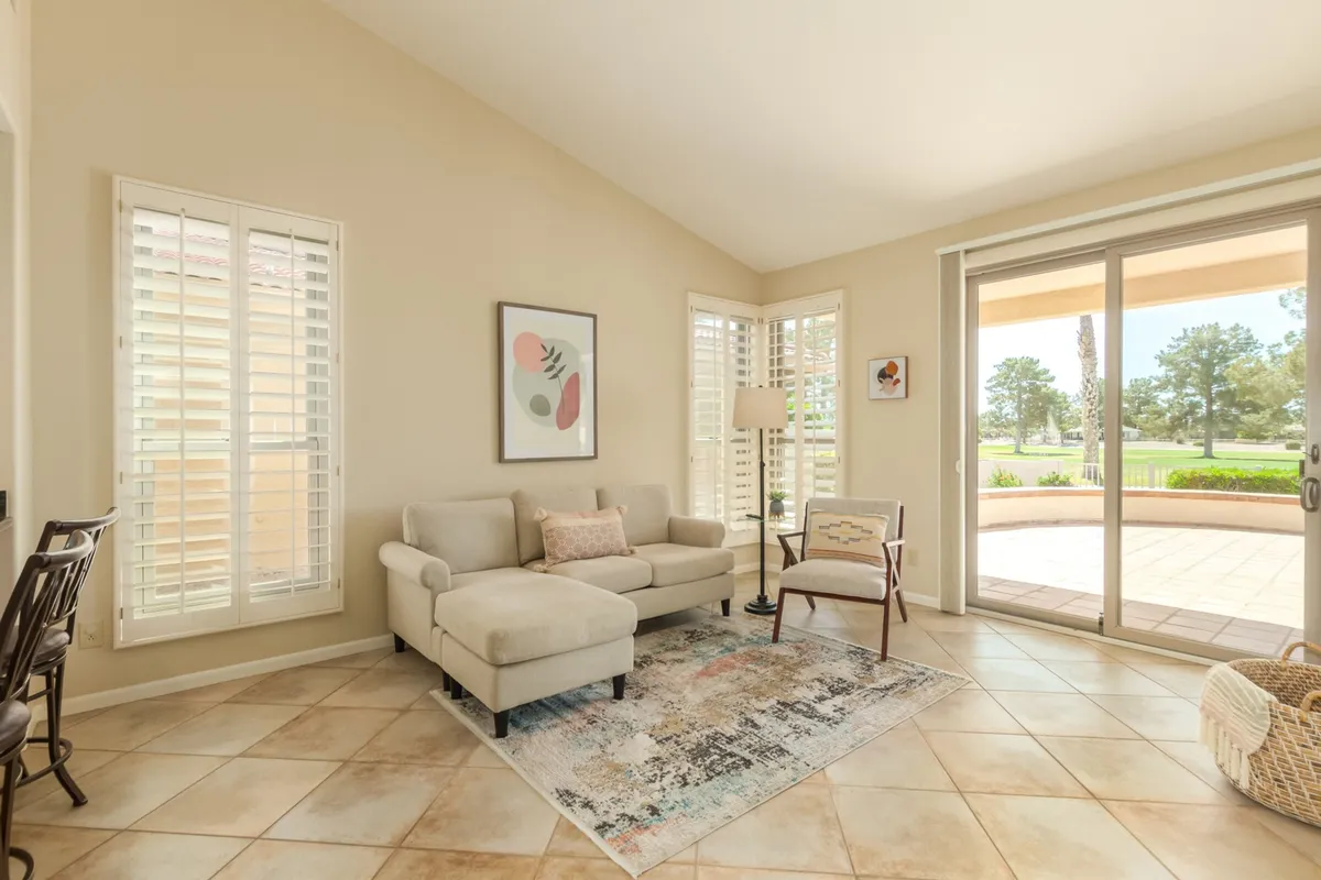A calm, welcoming living space with a sofa, artwork, rug, and a large sliding glass door revealing lush outdoor views. The setting is perfect for socializing, reading, or enjoying sunset views, with a cozy ambiance that invites togetherness.