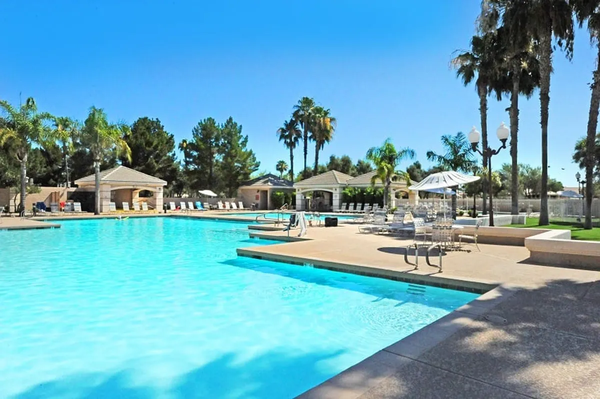 A sparkling swimming pool is surrounded by palm trees, lounge chairs, and cabana structures, inviting guests to unwind, swim, sunbathe, and gather with friends. The scene is relaxed yet lively, representing the resort-style amenities available to guests.