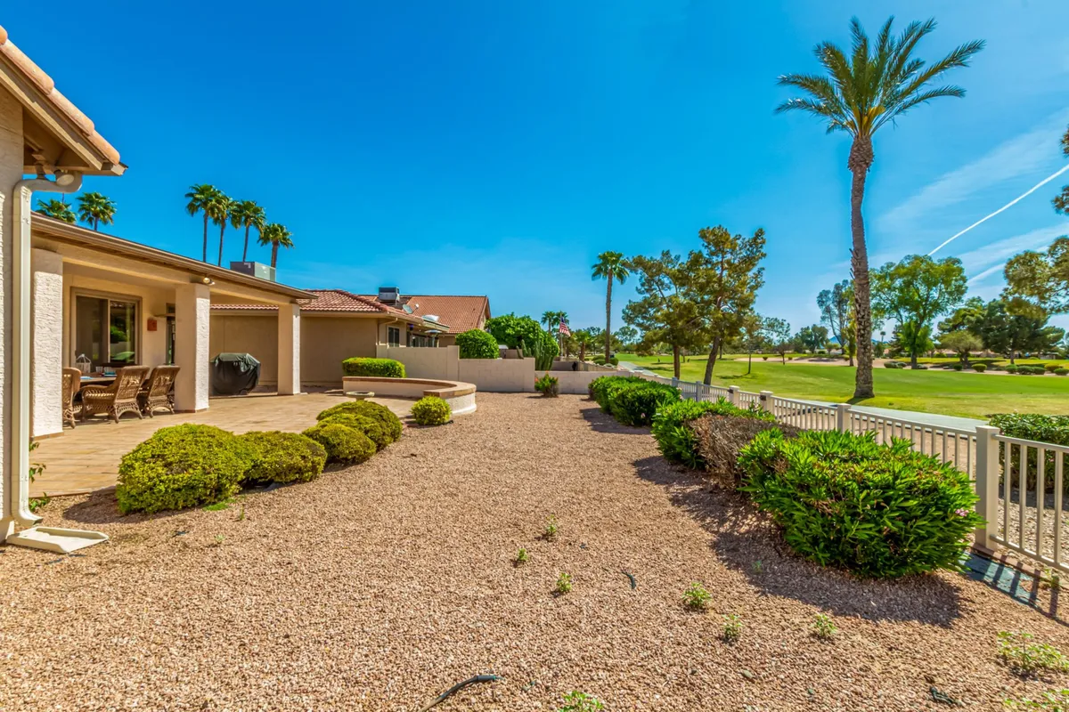 An expansive patio area faces the golf course, surrounded by lush greenery and tall palm trees. A well-appointed outdoor dining area offers a front-row seat to sunset views over the fairway, inviting guests to relax or host gatherings in the tranquil outdoor environment.