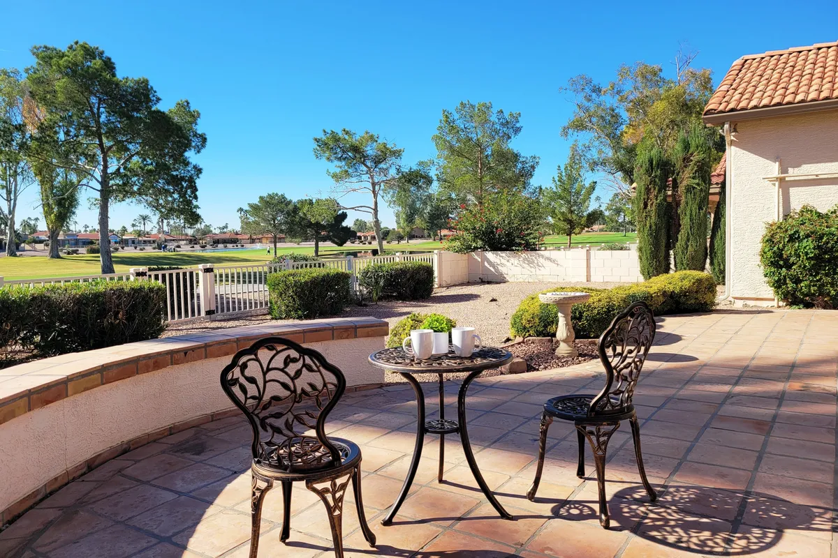A charming exterior patio setting featuring a bistro table and chairs overlooking the golf course, surrounded by greenery. The space is ideal for morning coffee, reading, or gathering with friends, offering relaxation and social connection.